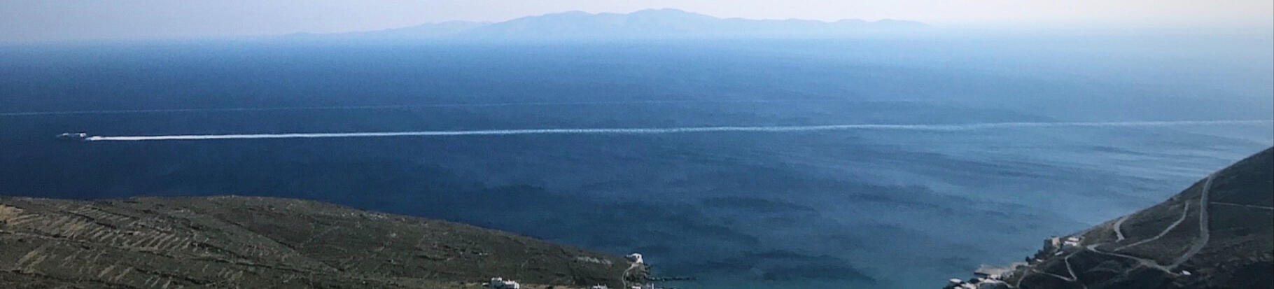 "A ferry speeds across the deep blue Aegean Sea near Tinos, Greece, leaving a white wake behind. A scenic view capturing the essence of island travel and adventure."