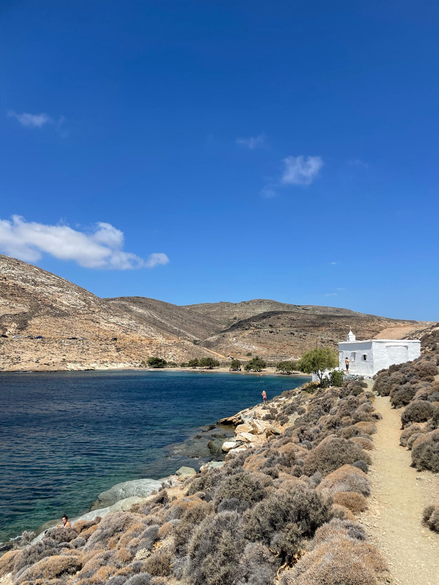 "A small white Cycladic church by the sea at Paralia Agia Thalassa, Tinos, Greece. Surrounded by rugged hills, it offers a peaceful retreat with stunning coastal views."