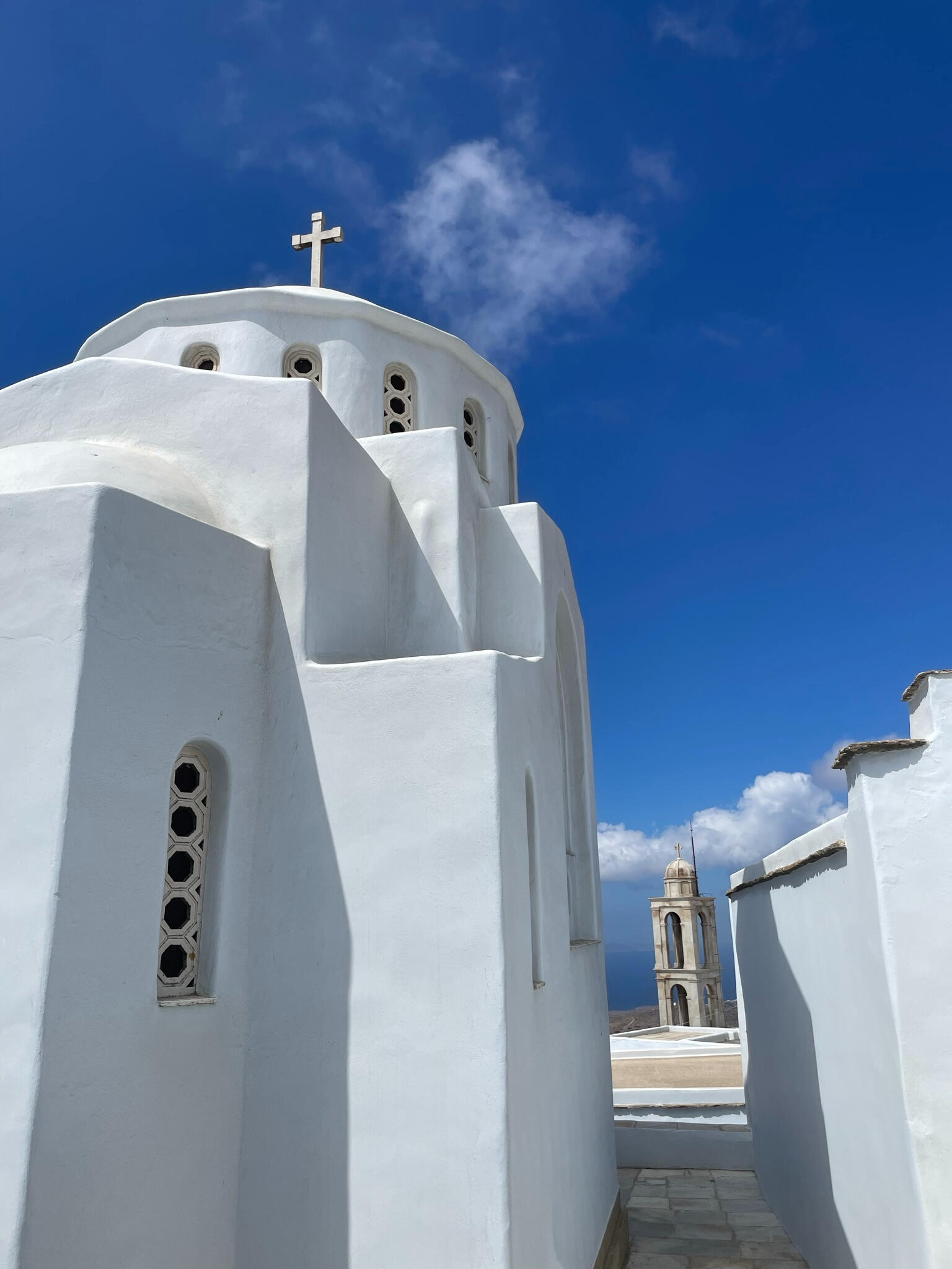 "A white Cycladic church on Tinos Island, Greece, with a blue sky backdrop. One of the island’s many historic chapels, reflecting its deep religious and architectural heritage."