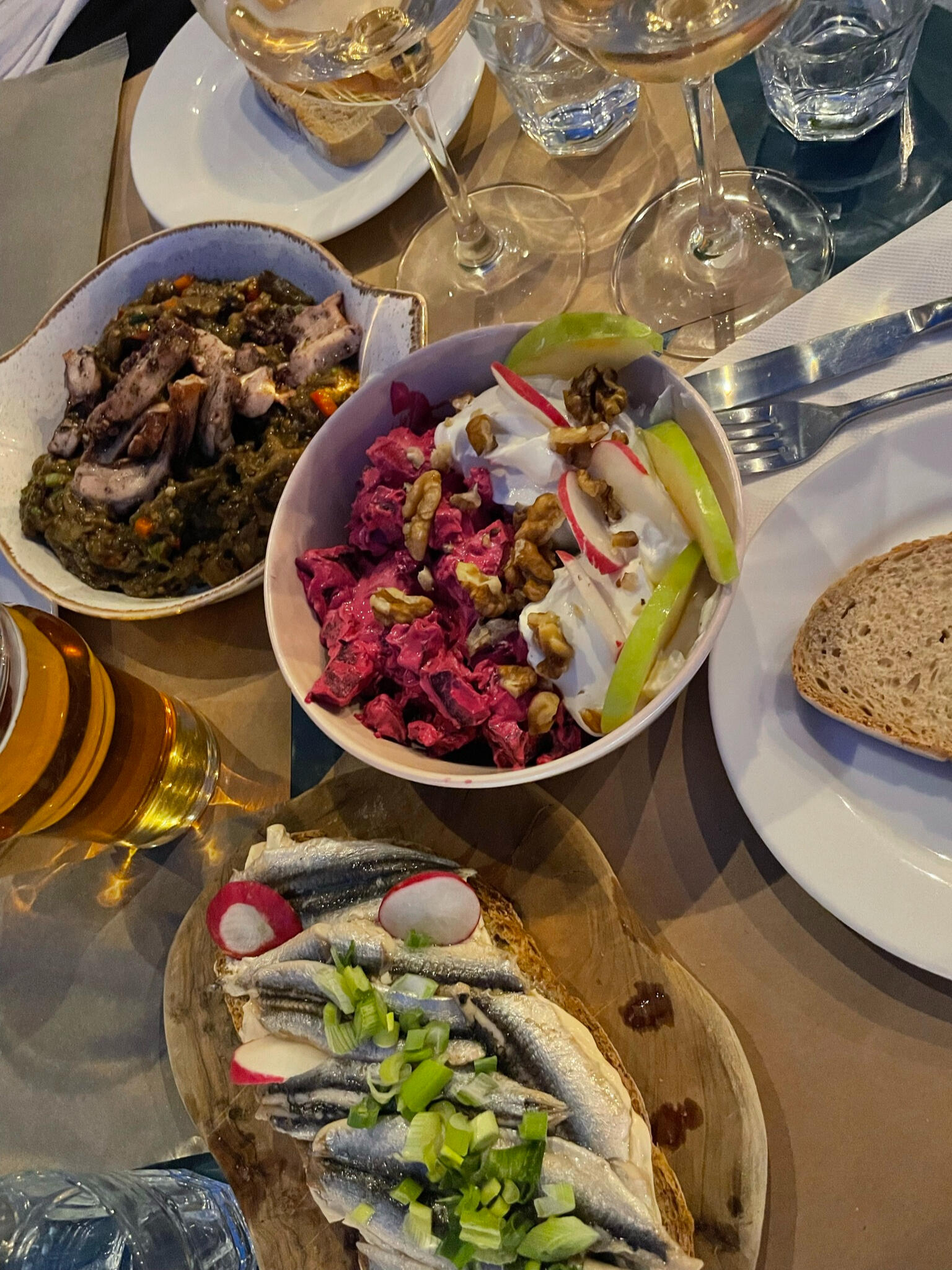 "A table filled with modern Greek cuisine in Tinos, Greece, featuring seafood, fresh salads, and local specialties, paired with wine and beer for a perfect meal."