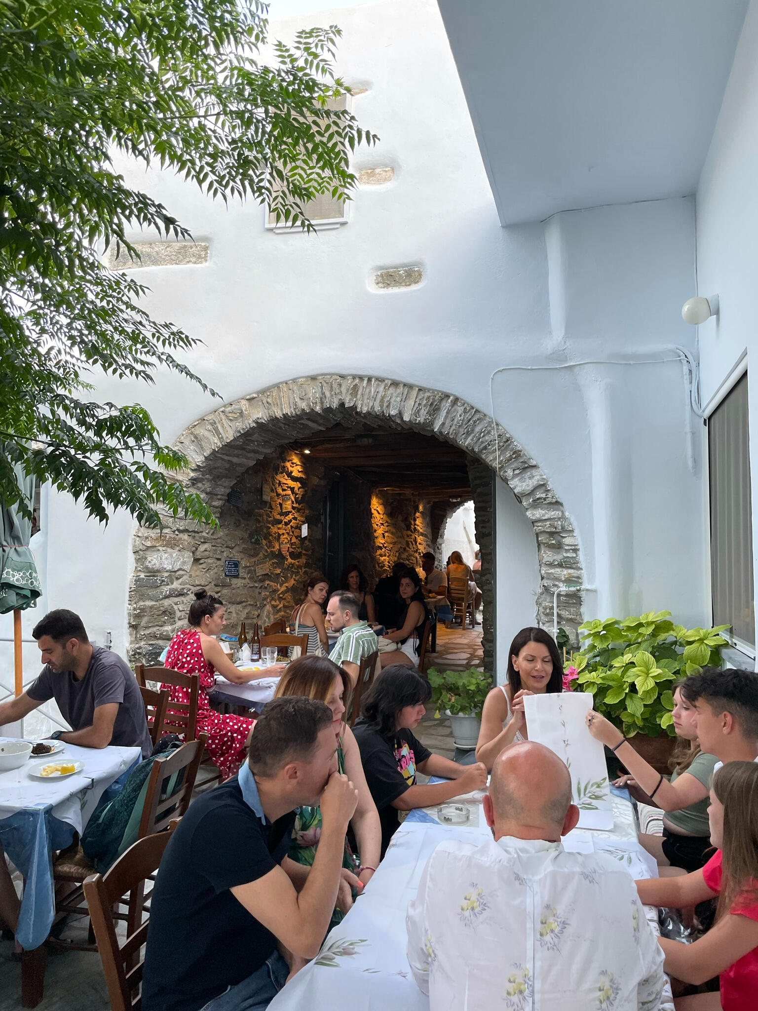 "Diners enjoy a meal at Teréza, a traditional Greek taverna in Tinos, Greece. The charming stone archway and courtyard create an inviting island dining experience."