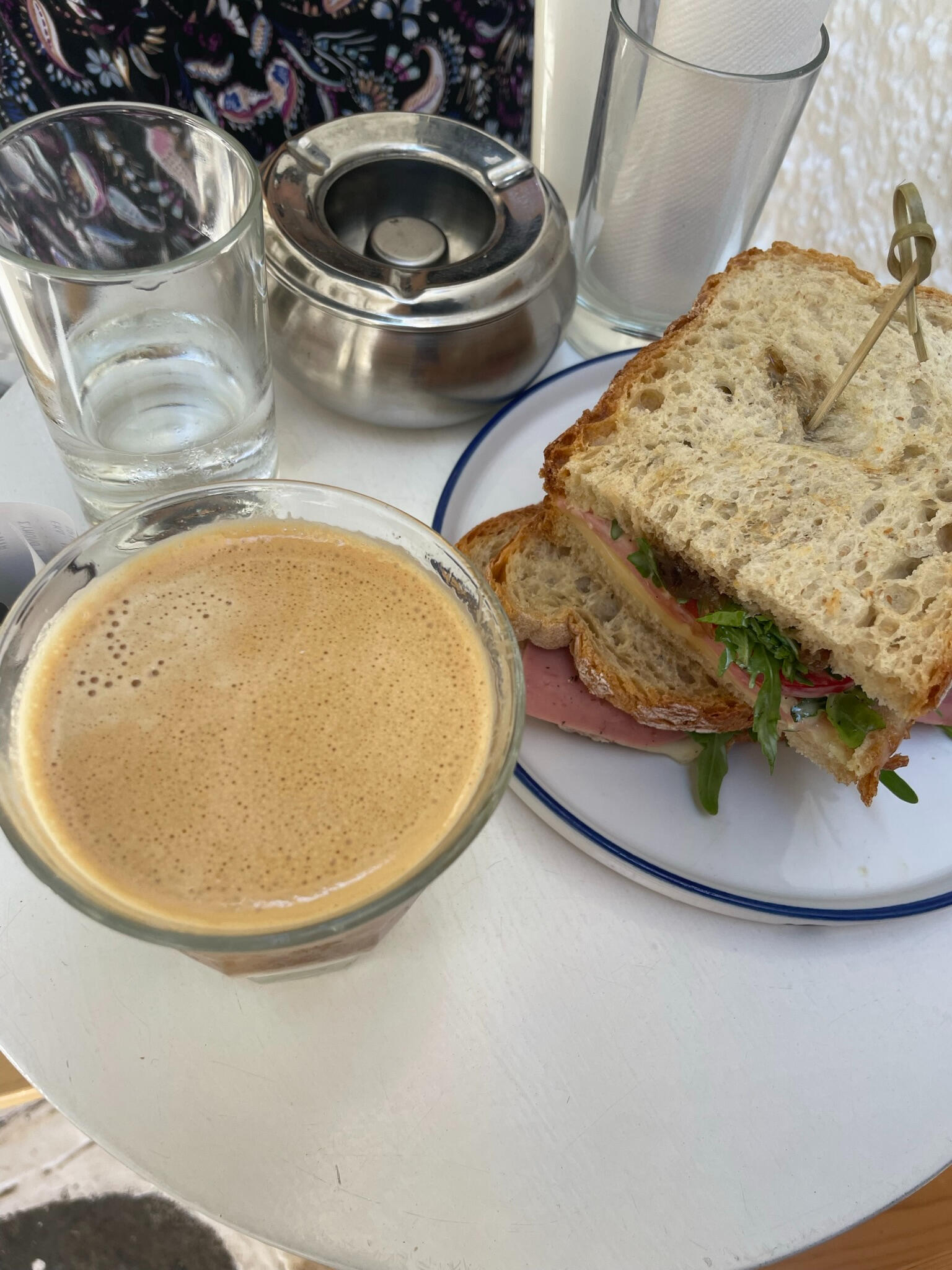 "A fresh sandwich with ham, greens, and wholegrain bread, served with a creamy coffee at Prickly Bear café in Tinos, Greece. A perfect island breakfast stop."